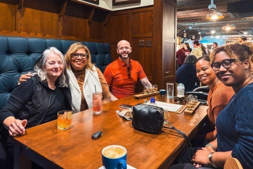 Un grupo de personas sentadas en una mesa de madera en un restaurante, con un banco acolchado azul al fondo. 4