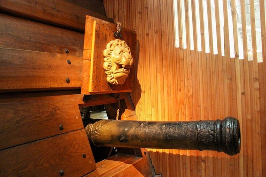 Un canon monté sur une structure en bois, ornée d’un emblème représentant une tête de lion. 3