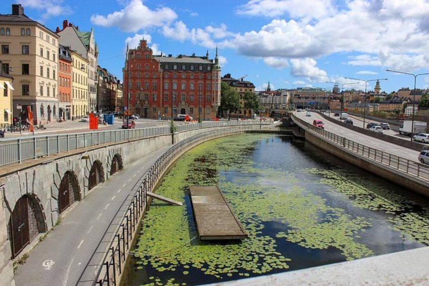 Un pont enjambant un plan d’eau parsemé de nénuphars, un bâtiment rouge et un ciel dégagé. 4