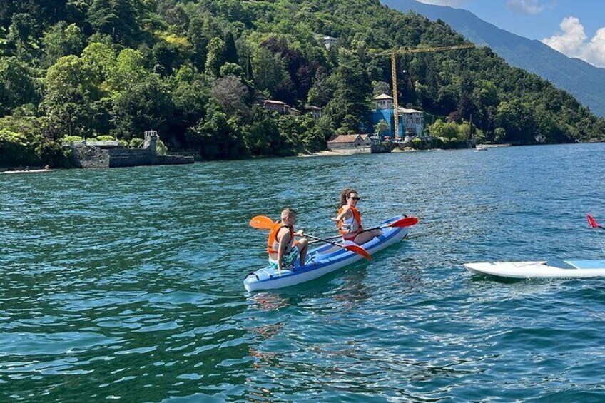 Two people kayaking on a calm lake surrounded by lush greenery and mountains. 2