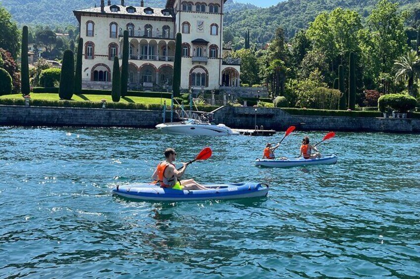 Three people kayaking on a calm lake with a grand building in the background. 1