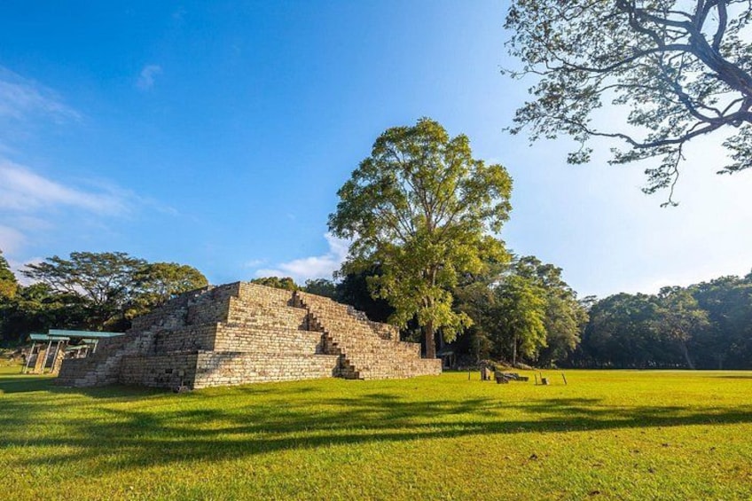 A stone pyramid structure in a grassy field with trees in the background. 5
