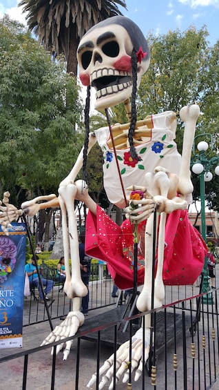 A skeleton sculpture with a skull head, dressed in a red skirt and holding a flower. 3