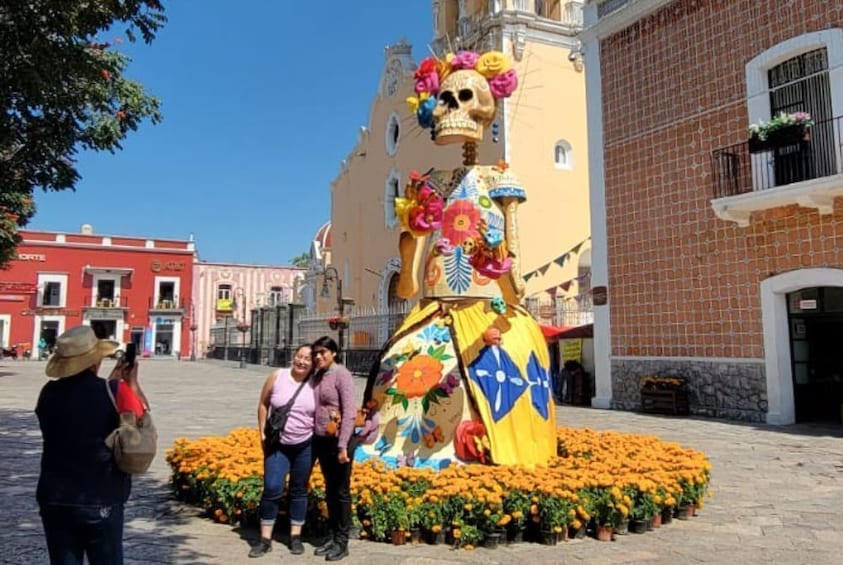 A large skeleton sculpture surrounded by marigold flowers in a plaza. 1