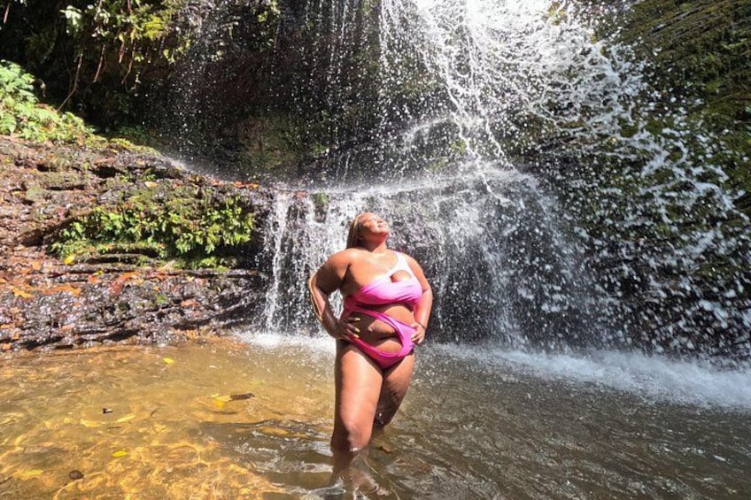 A person in a pink bikini standing in a shallow water area with a waterfall in the background. 3