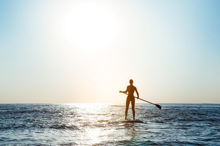 A person paddleboarding on calm water during sunset. 4