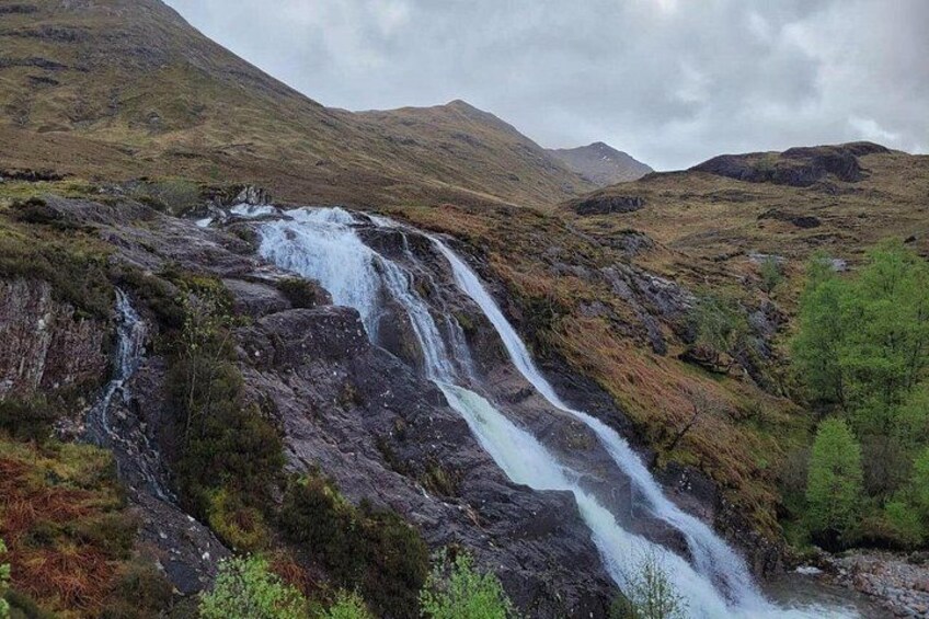 A waterfall cascading down a rocky hillside surrounded by green vegetation and hills. 2