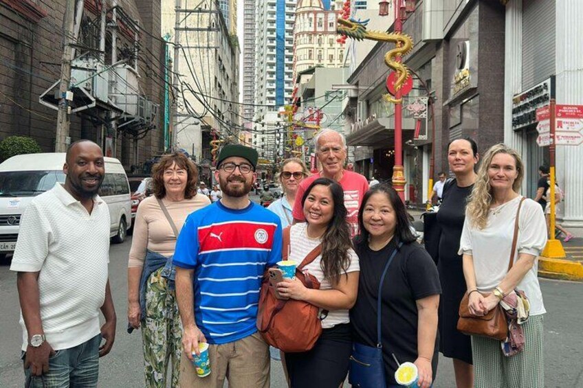 A group of people standing on a city street with buildings and a decorative structure in the background. 4