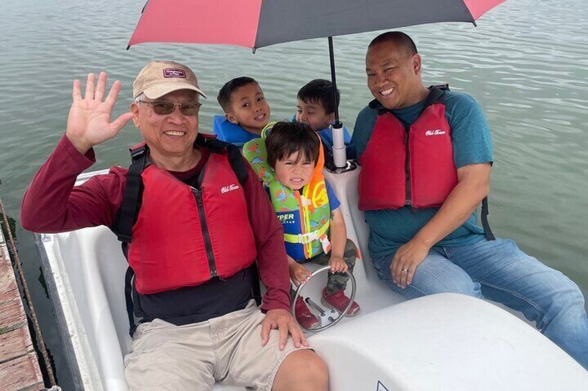 A man and a child on a boat, both wearing red life jackets, with an umbrella above them. 5