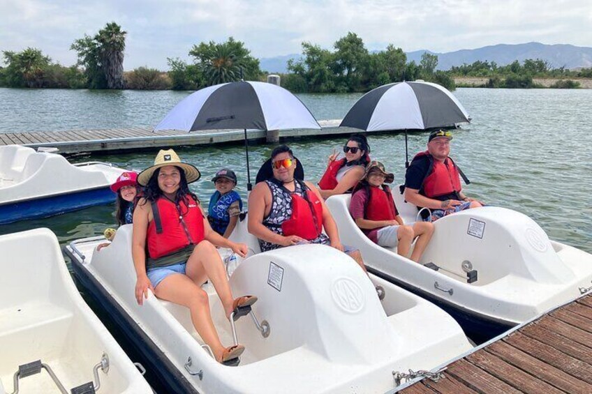 People on a boat with life jackets, a dock, and a calm lake with trees and mountains in the background. 1