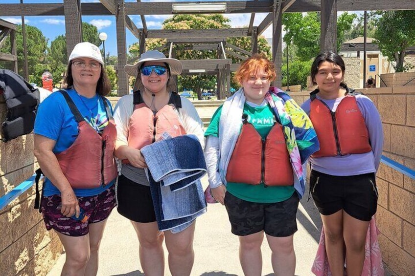 Four people wearing life jackets and carrying backpacks, standing under a wooden structure. 2