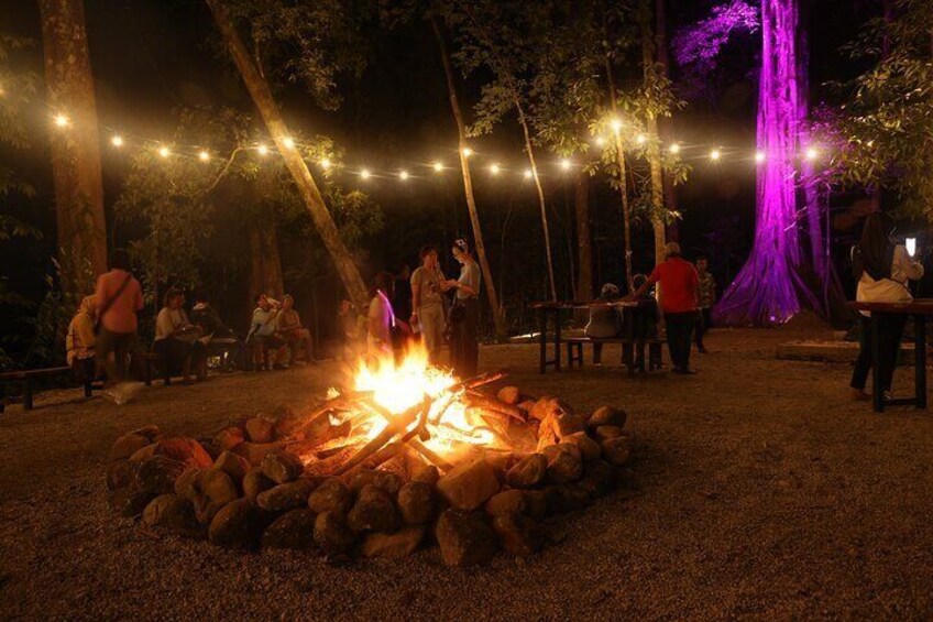 A campfire surrounded by rocks, string lights, and people gathered around. 4