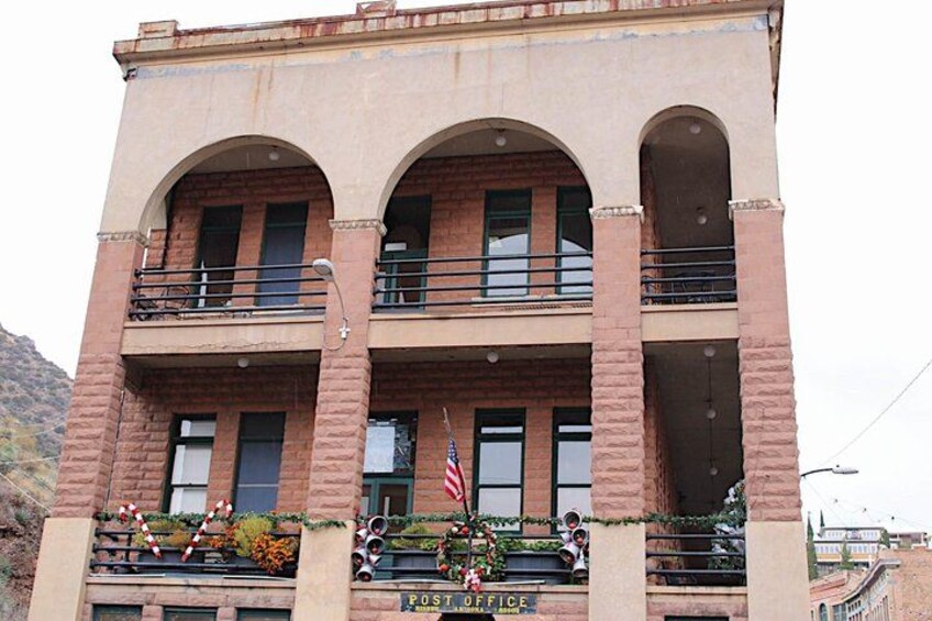 A two-story building with a balcony, a flag, and a sign that reads 'POST OFFICE.' 5