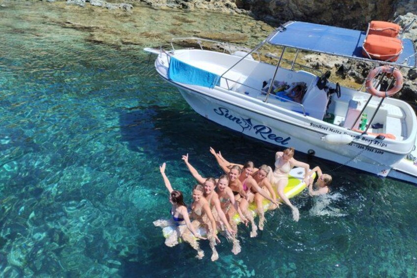 A group of people on a boat with clear water, a rocky shore, and a lifebuoy. 1