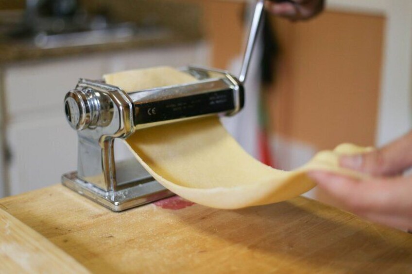 Una persona usando una máquina para hacer pasta y estirar masa sobre una superficie de madera. 5