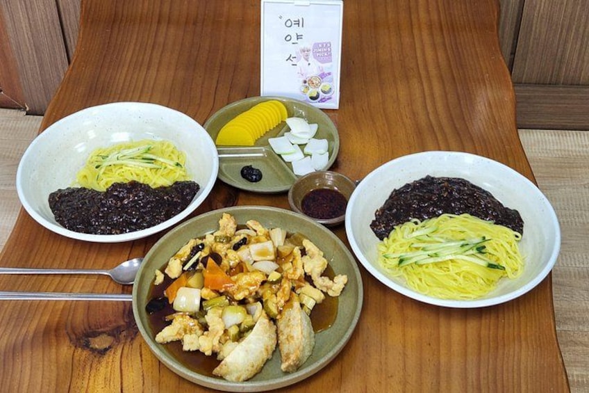 A wooden table with various dishes including noodles, vegetables, and a bowl of soup. 5