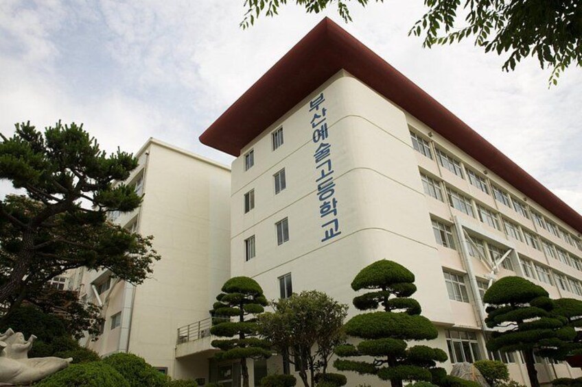 A multi-story building with a red roof and white walls, surrounded by neatly trimmed trees. 4