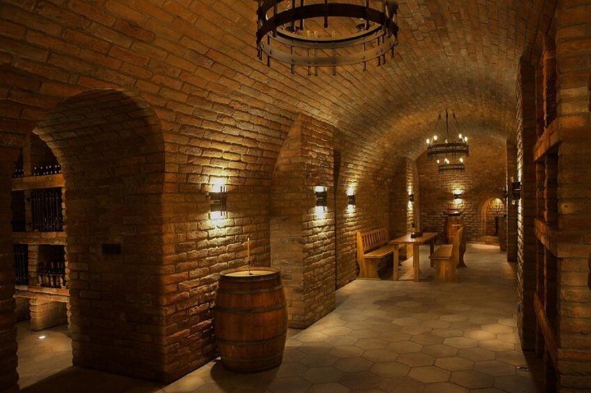 A brick-walled corridor with hexagonal tiles, wooden benches, and a large barrel. 1