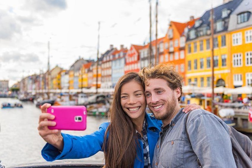 Una pareja se toma un selfie con un teléfono rosa, un río y edificios coloridos al fondo. 4