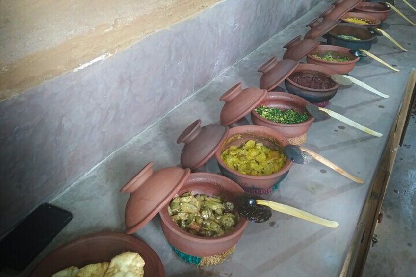 Une rangée de pots en argile, dont certains sont recouverts de couvercles et contiennent de la nourriture, est posée sur un sol carrelé. 4