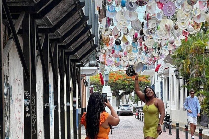 A street with a unique ceiling of hanging plates, a pedestrian, and a parked car. 1