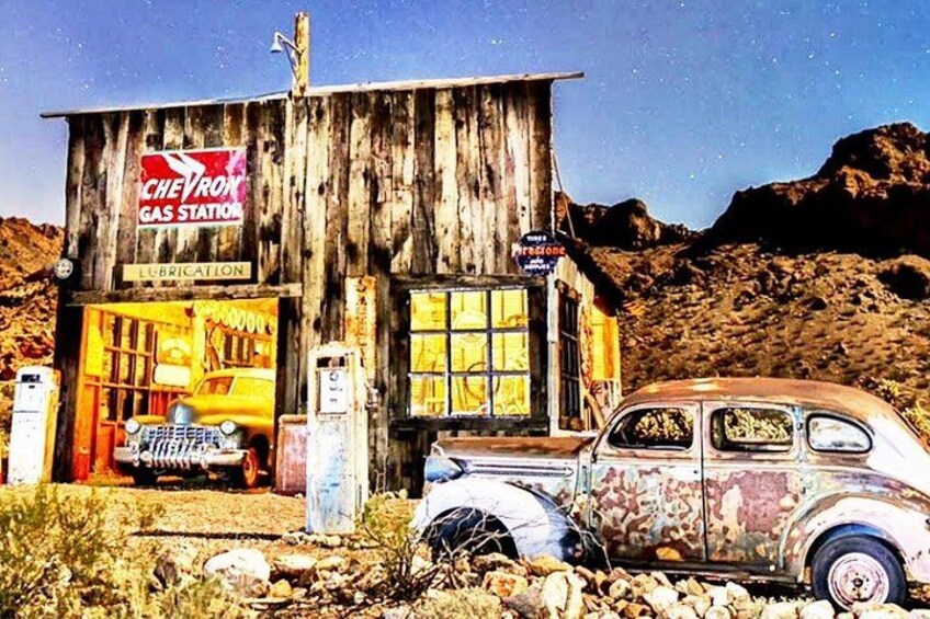 A vintage car parked in front of a wooden gas station with a Chevron sign. 1