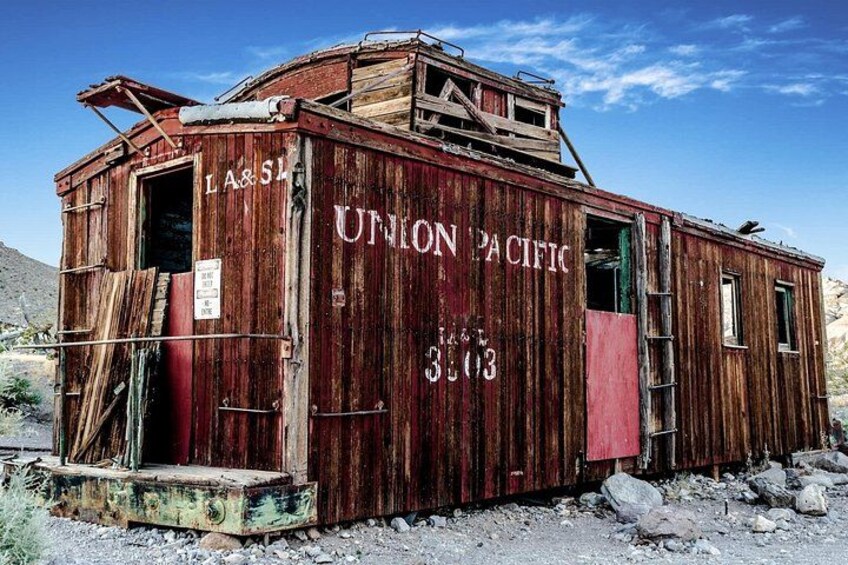A dilapidated wooden building with 'Union Pacific' and 'LA&S' written on it, located in a desert-like environment. 2