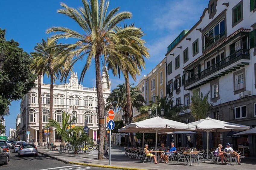 A street with palm trees, a stop sign, and outdoor seating at cafes. 4