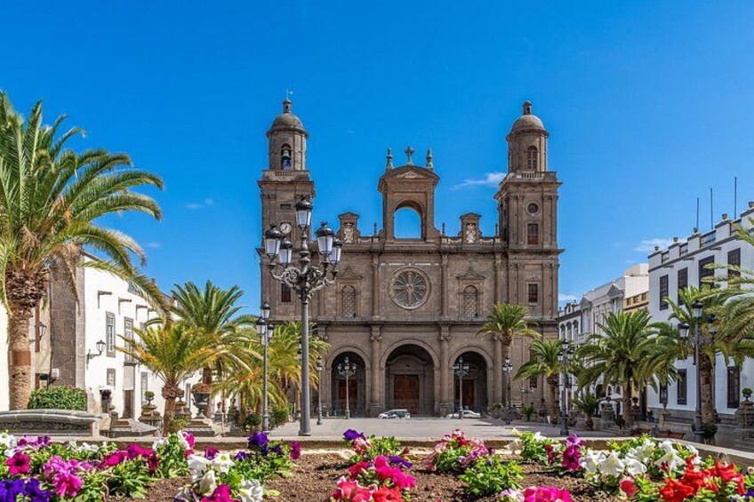 A historic church with two bell towers, surrounded by palm trees and colorful flowers. 1