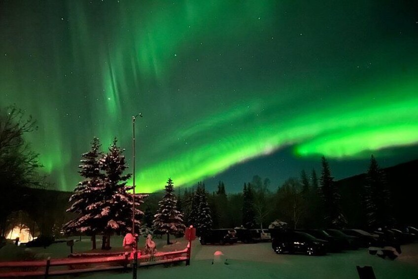 Schneebedeckte Landschaft mit grüner Polarlichterscheinung, Bäumen und einem Auto. 1
