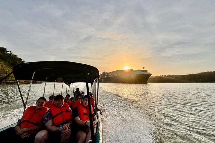 Un bote con pasajeros usando chalecos salvavidas, un barco grande al fondo y un atardecer. 2