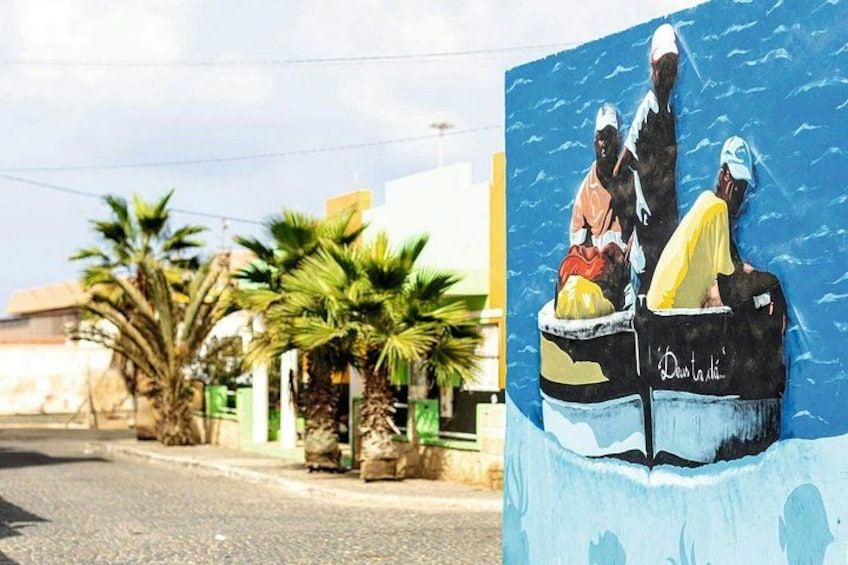 Une rue bordée de palmiers et ornée d’une fresque représentant des personnes à bord d’un bateau. 2