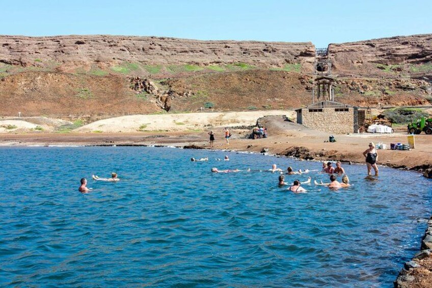A coastal area with people swimming in the water, a rocky shoreline, and a small building. 5