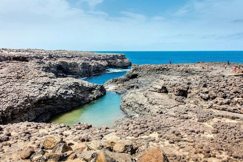 Un paysage côtier rocheux, avec une mer d’un bleu limpide, un étroit canal d’eau et une côte lointaine. 4