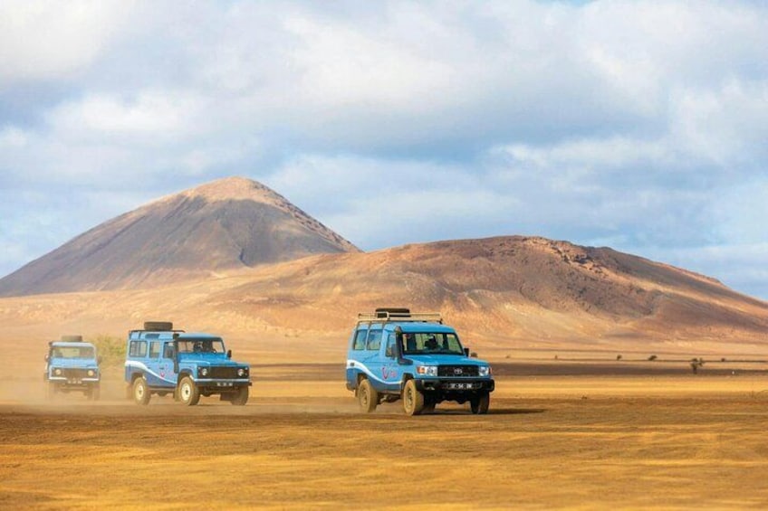 Three blue safari vehicles on a dirt road with a mountain in the background. 1
