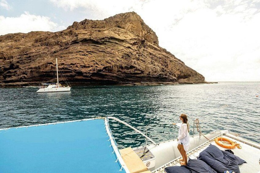 A person on a boat near a rocky coastline with a sailboat in the distance. 3