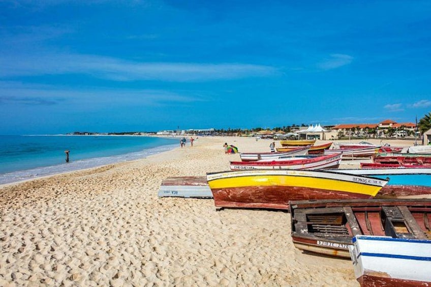 A beach with boats, a clear sky, and a distant shoreline with buildings. 2