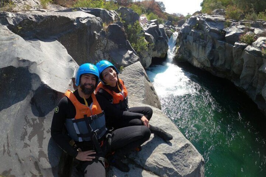 Due persone con caschi e giubbotti di salvataggio sedute su una roccia vicino a un fiume. 1