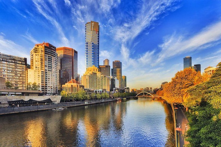 A city skyline with a river, modern buildings, and autumn trees. 2