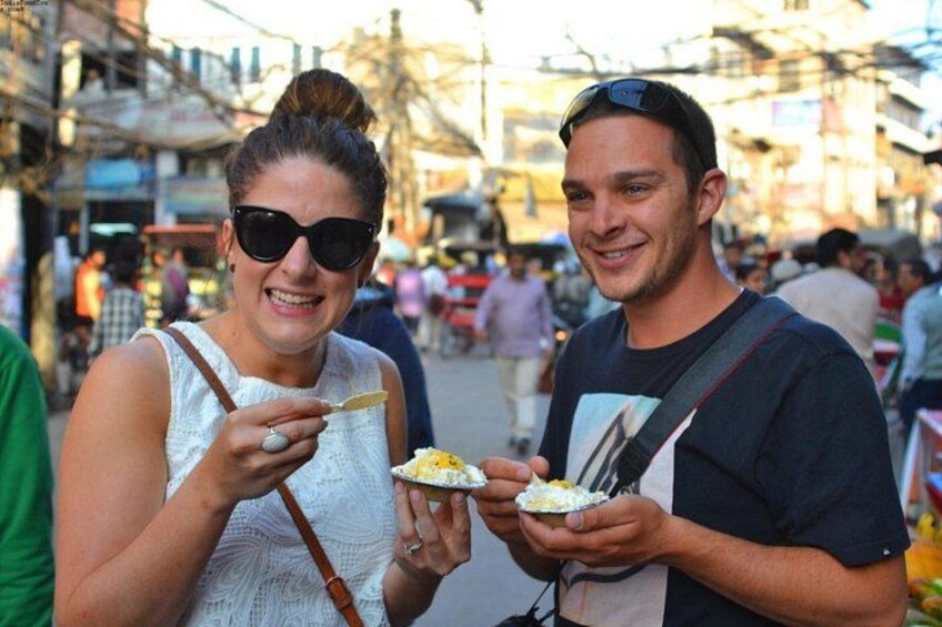 Two people holding plates of food in an outdoor market setting. 3