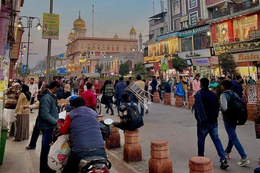 Una calle concurrida con gente caminando, tiendas y un edificio grande con cúpulas. 5