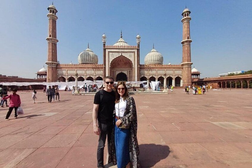 Un gran edificio histórico con cúpulas y minaretes, un patio empedrado y gente caminando. 1