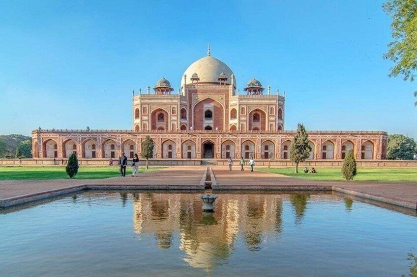 A large, historic building with a central dome and multiple smaller domes, surrounded by a reflective water body and a well-maintained garden. 2