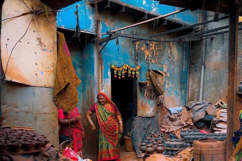 Una vivace scena di mercato rustico, con una donna in abiti tradizionali, un edificio blu e diversi oggetti domestici. 1