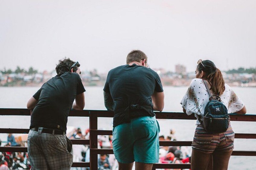 Three people standing by a railing, overlooking a body of water with buildings in the background. 2