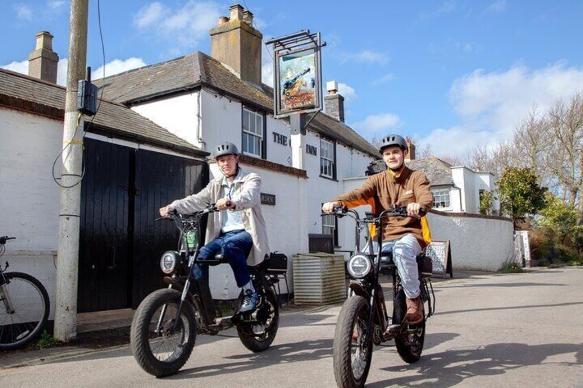Two people riding bicycles on a street with a pub in the background. 4