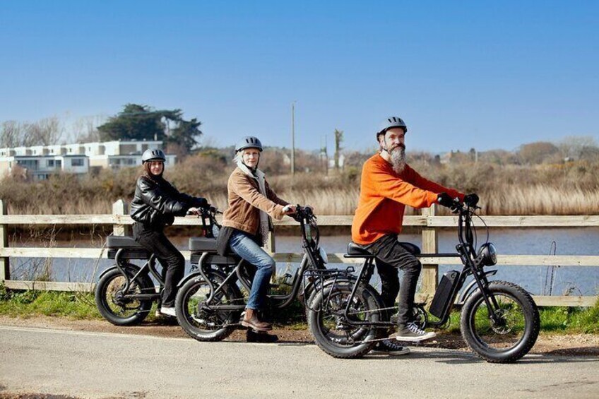Three people riding bicycles on a paved path near a body of water. 5