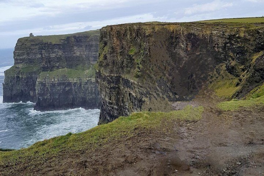 A coastal cliff with a grassy path leading to a lighthouse. 2
