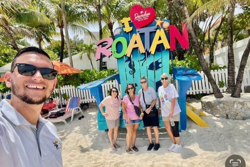 A beach with a colorful sign that reads 'ROATAN' and a palm tree in the background. 5