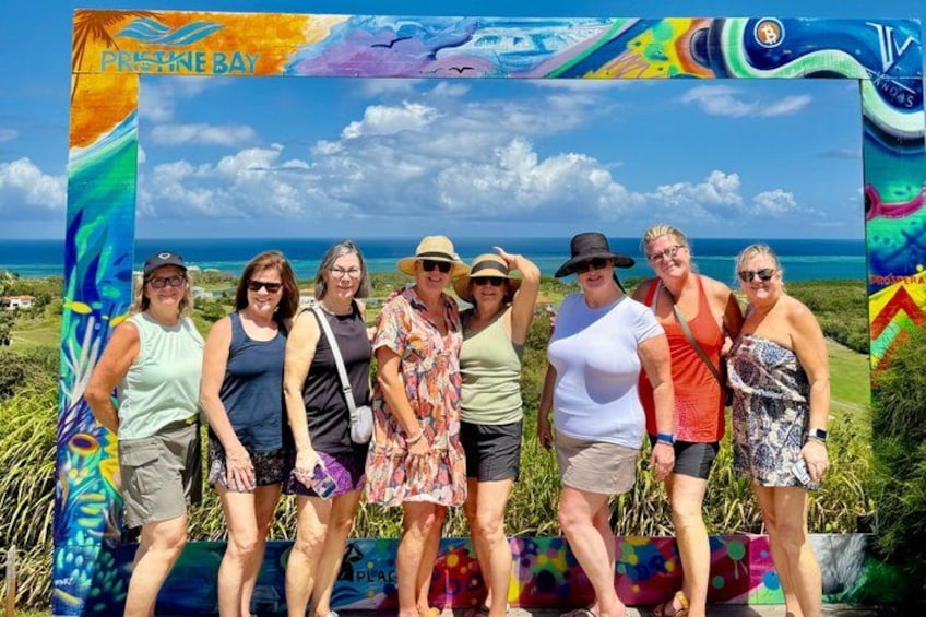 A group of people standing in front of a colorful backdrop with the text 'PRESTONE BAY' and a scenic view of the ocean. 3